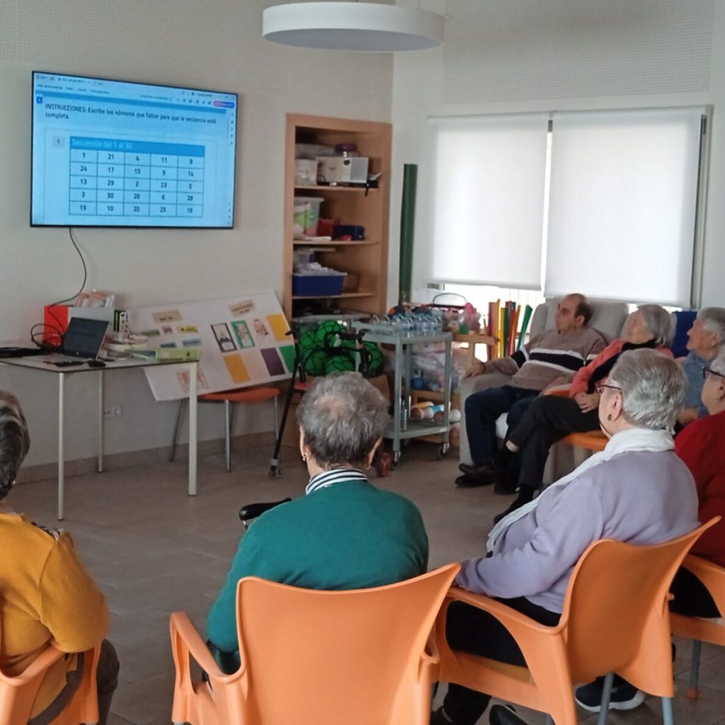 Usuarios realizando una actividad de estimulación cognitiva con una terapeuta y una pantalla digital en AFA Castalla y Onil.